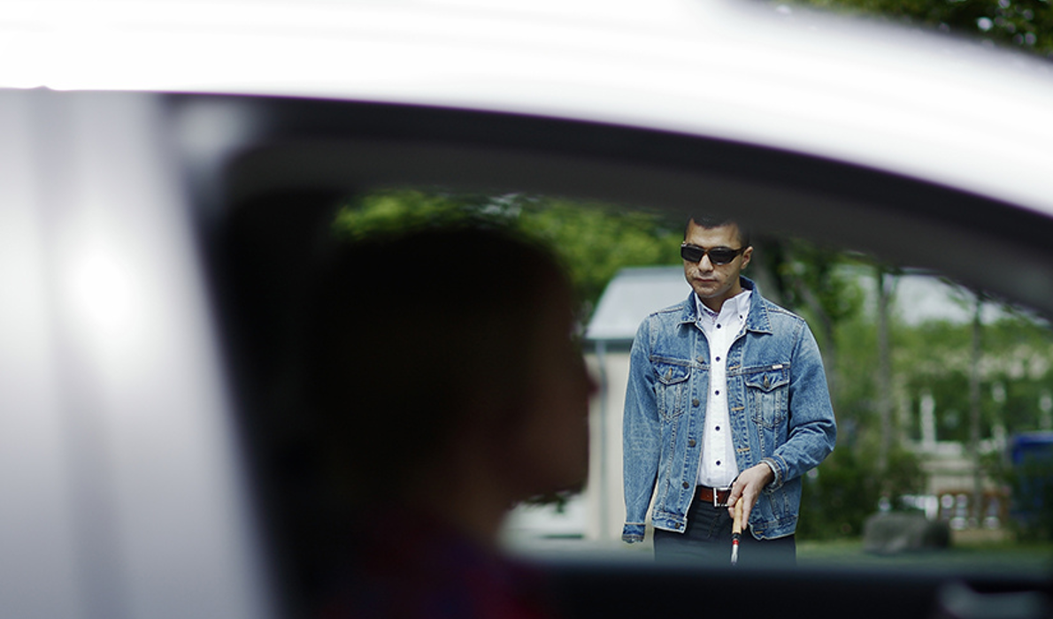 synskadad person med vit käpp går mot en bil