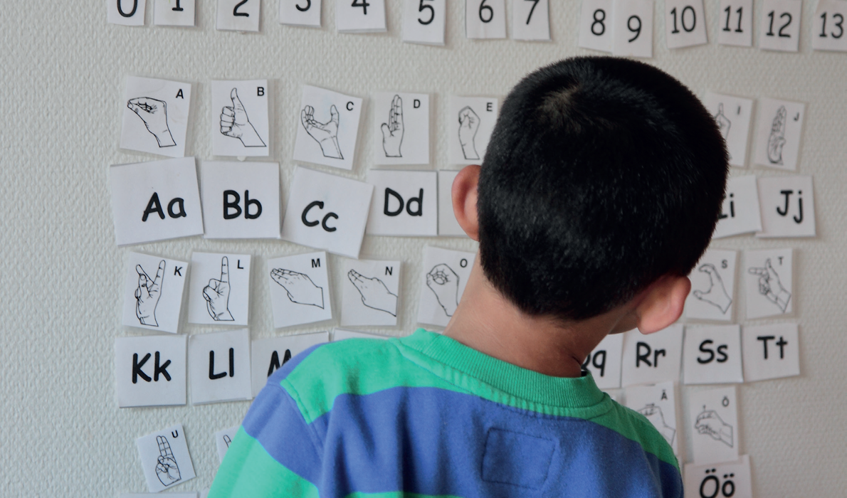 Pojke vänd mot en vägg och tittar på teckenspråksbilder av alfabetet